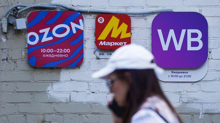 Nainen kävelee etualalla, taustalla näkyy Ozon, Yandex Market ja WIldberries -yritysten mainoskyltit.
