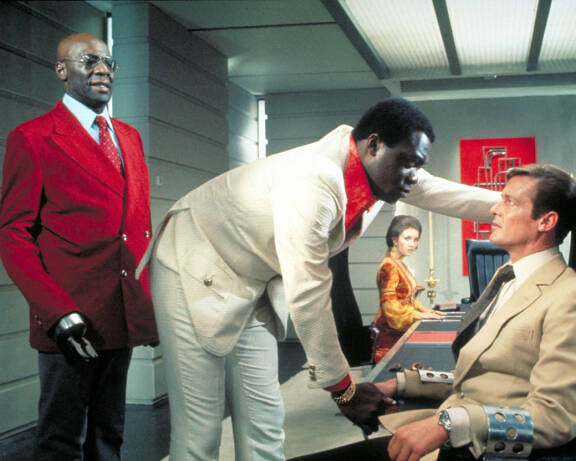 Tee-Hee (Julius Harris, vas.) on tohtori Kanangan (Yaphet Kotto) kätyri. Oikealla James Bond (Roger Moore). Taustalla Jane Seymourin esittämä Solitaire.
