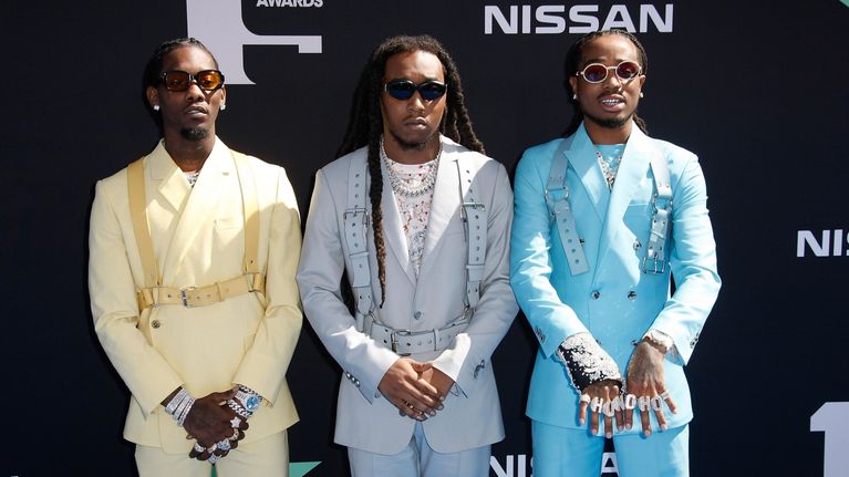 Kolme miestä seisoo vierekkäin juhlapuvuissa mustan seinän edessä, taustalla tekstit "BET AWARDS" ja "NISSAN".