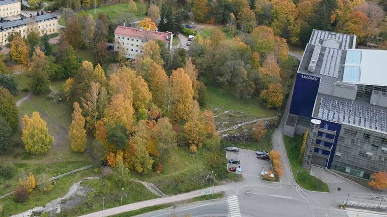Ilmakuva puistosta, jonka laidalla toimistorakennus ja parkkipaikka.
