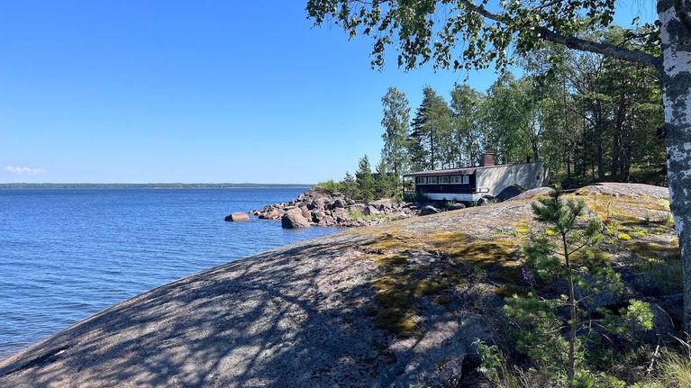 Saari, jonka rannalla on rakennus. Etualalla on kalliota.