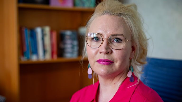 Vaaleahiuksinen nainen katsoo kohti.