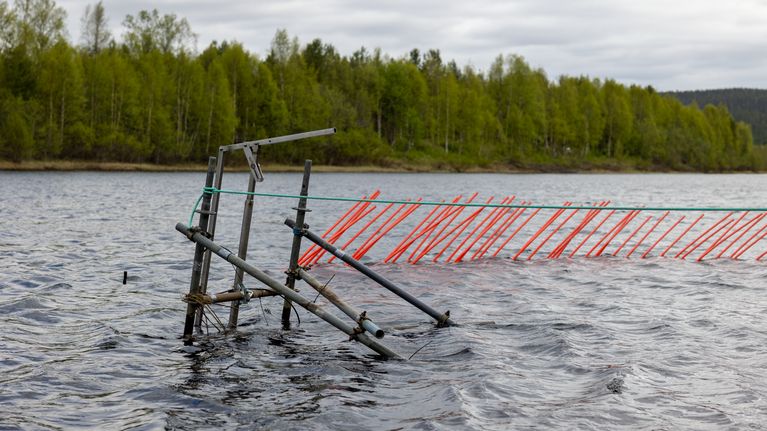 Kaikuluotaimen metallikehikko nousee vedenpinnan yläpuolelle jokivarressa keväisessä maisemassa.