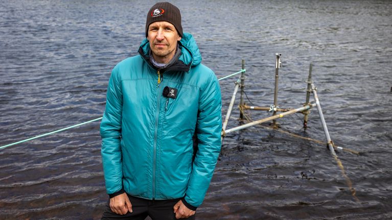 Tutkija seuraa vesistön mittauslaitteiston toimivuutta joen rannalla. +