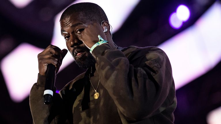 Kanye West tummanvihreässä paidassa pitää mikrofonia. Hän nostaa nyrkit kasvojensa eteen.