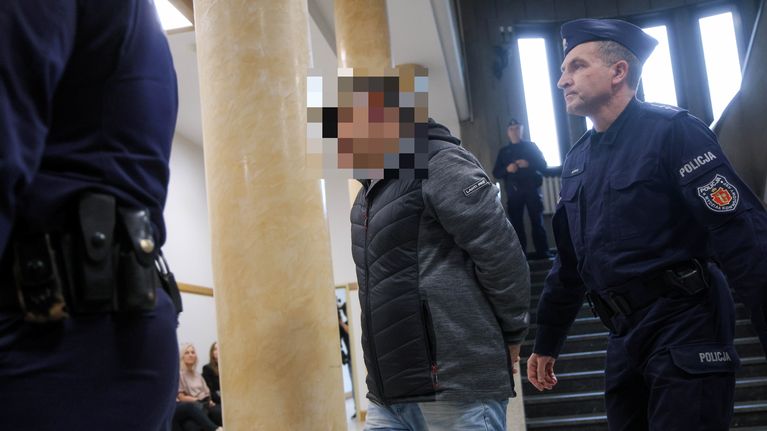 Siniunivormuinen poliisi saattaa miestä oikeustalolla. Miehellä on farkut ja toppatakki. Hänen kasvonsa on pikselöity.