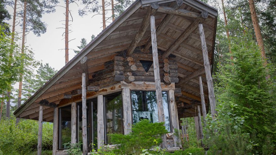 Hirsirakenteinen saunamökki metsäisessä ympäristössä, ikkunat heijastavat puita.