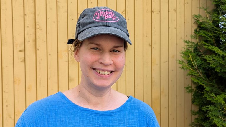 Nuori nainen seisoo keltaisen puuseinän edessä päässään nylon beat hattu.