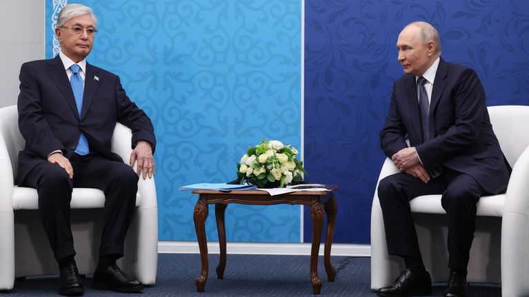 Tokajev ja Putin istuvat valkoisilla tuoleilla pienen pöydän molemmin puolin. Miehillä on mustat puvut ja siniset kravatit.