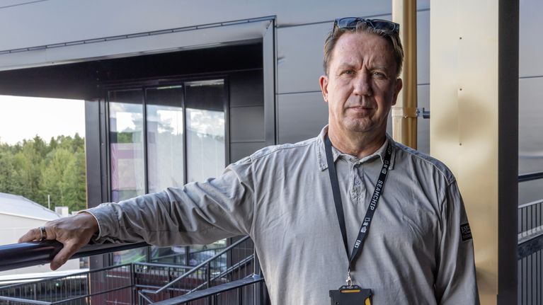 Mies katsoo suoraan kameraan. Kaulassa henkilökortti.