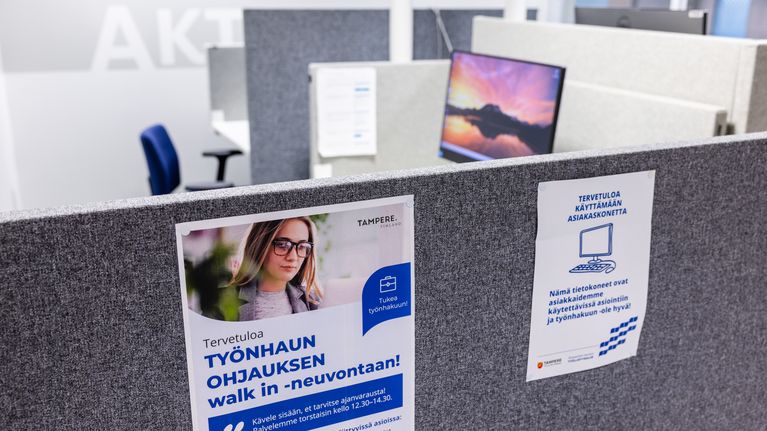Toimistotilassa harmaiden väliseinien pinnalla on kaksi esillä julistetta, joissa kerrotaan työnhaun ohjauksesta.