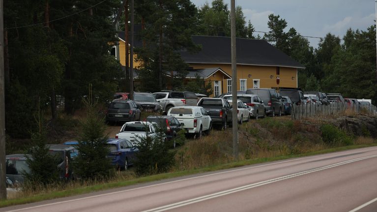 Keltainen, harmaakattoinen talo, jonka pihalla on kymmeniä autoja. Ympärillä puita.