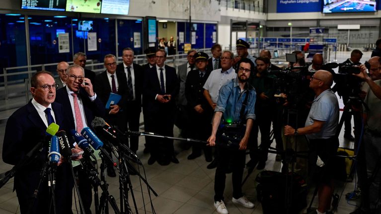 Saksan sisäministeri Alexander Dobrindt puhuu lehdistölle lentoasemalla. Hänen edessään on runsaasti mikrofoneja.