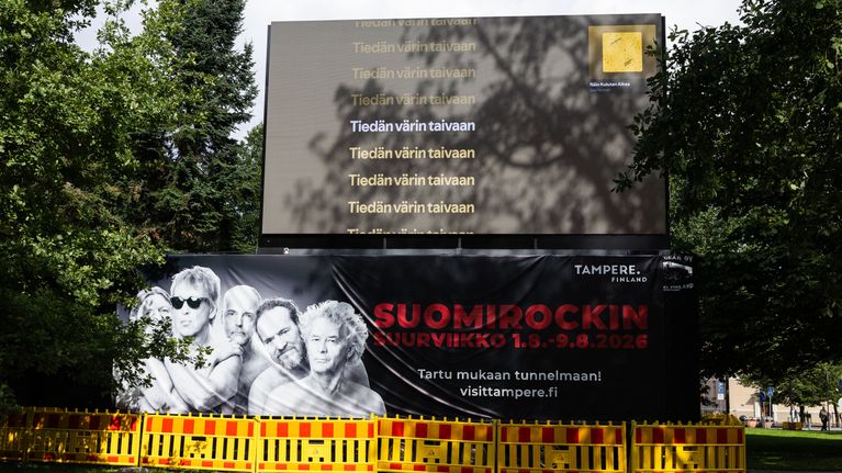 Ulkomainostaulu Tampereella, näytöllä mustalla pohjalla valkoista ja keltaista suomenkielistä tekstiä Eppu Normaalin Näin kulutan aikaa-kappaleesta.