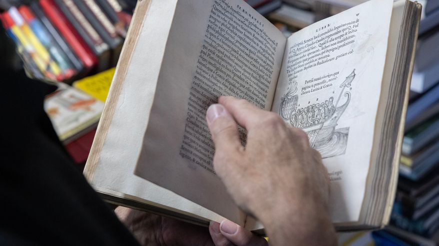 Henkilö selaa vanhaa kirjaa, jossa on mustavalkoinen piirros vanhasta laivasta.