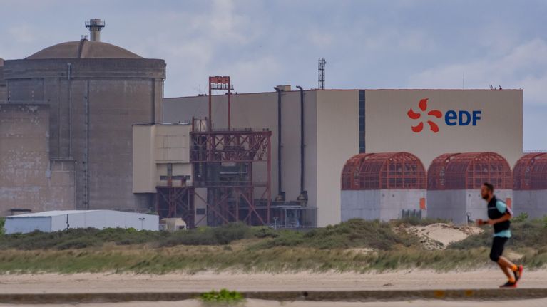 Etualalla henkilö lenkkeilee hiekkatiellä, taustalla suuri teollisuusrakennus, jonka seinässä lukee ”EDF.