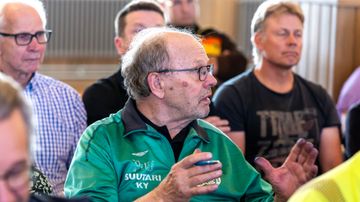 Vihreäpaitainen mies puhuu yleisön joukosta.