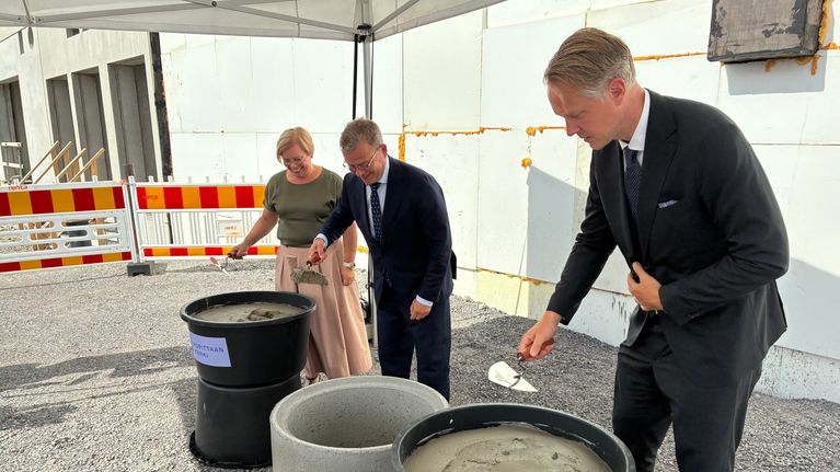 Pääministeri Petteri Orpo ja kaksi muuta henkilöä laastikauhat kädessä peruskiven muuraustilaisuudessa.