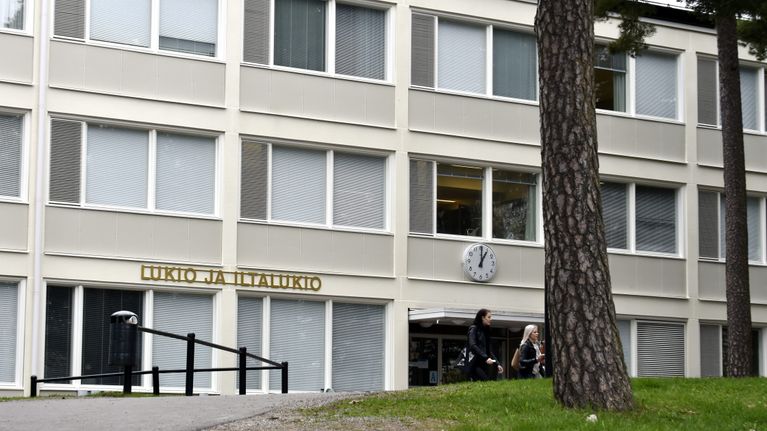 Lohjan yhteislyseon lukion rakennus kahden paksun männynrungon takaa kuvattuna.