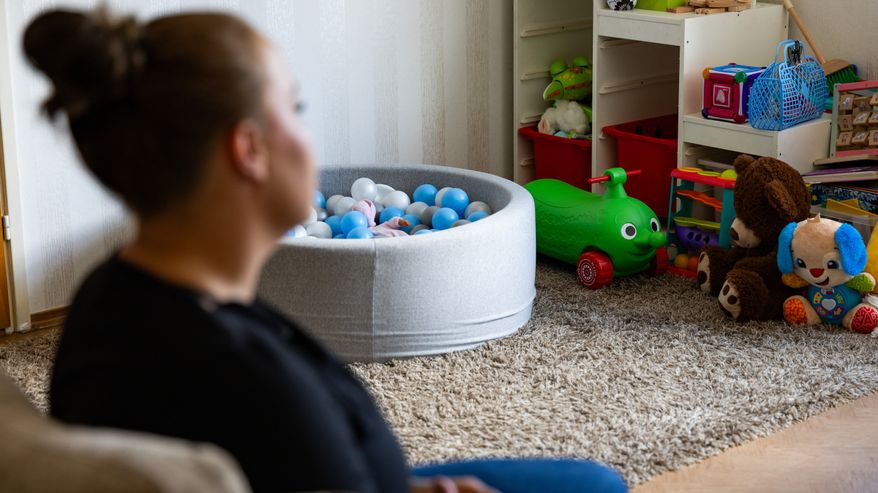 Työtön Riina Kahari istuu sohvalla ja taustalla näkyy pieni lasten pallomeri, sekä klassikkolelu: kurkkumopo.