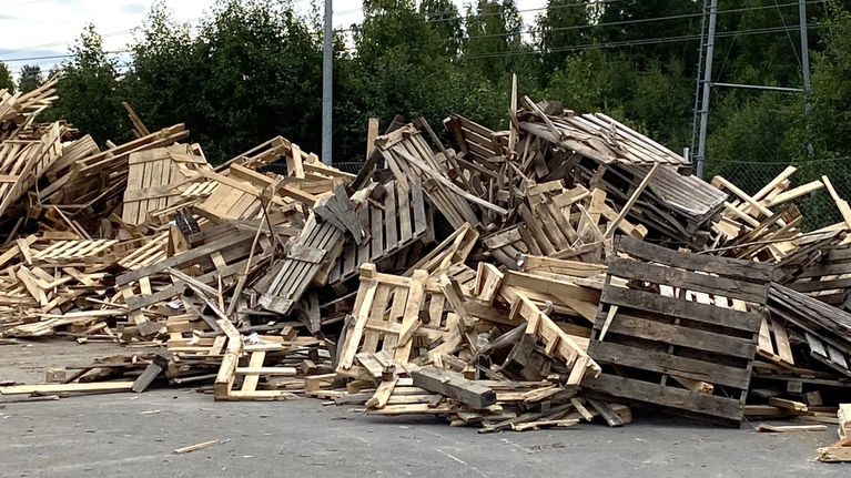 Asfalttikentällä on suuri kasa käytettyjä, puisia kuormalavoja.