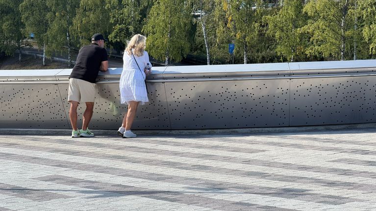 Mies ja nainen nojaavat kävelysillan kaitseeseen ja katsovat maisemia.