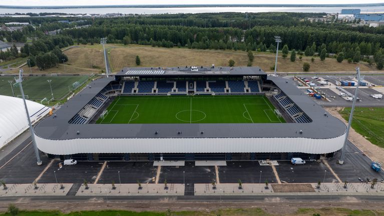 Jalkapallostadion viheriöineen ja katsomoineen, taustalla metsäalue ja merenrantaa.