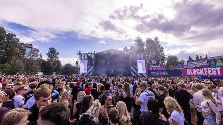 Suuria ihmisjoukkoja ulkoilmakonsertissa lavan edessä, lavalla savua ja lavan vieressä kontti, jossa teksti Blockfest.