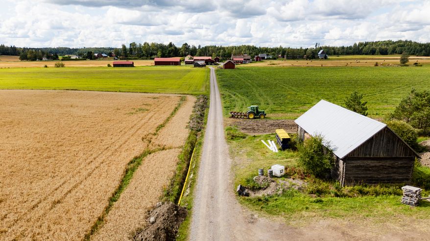 Soratie jakaa viljapellot, oikealla lato ja traktori pellolla, taustalla maatilan rakennuksia.