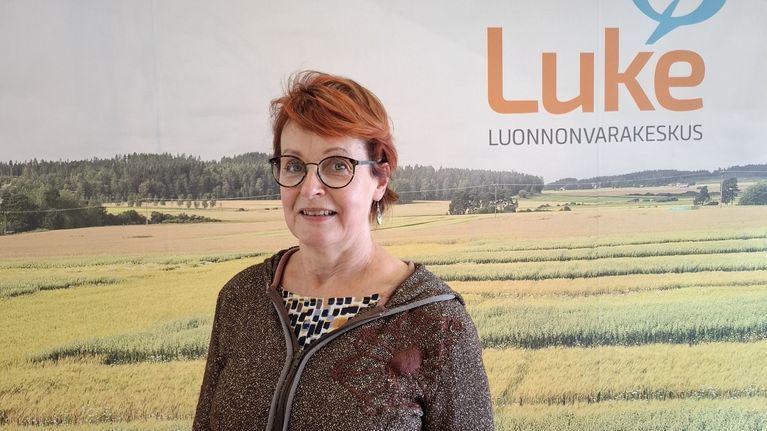 Luonnonvarakeskuksen logon edessä seisoo nainen.
