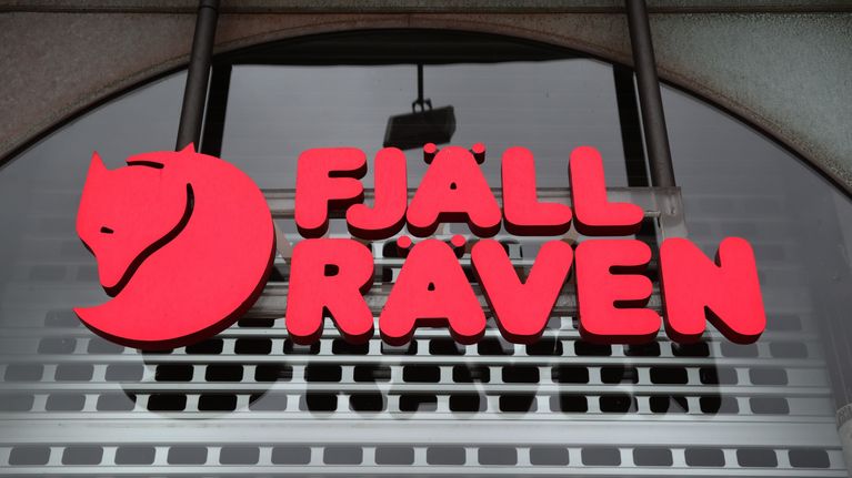 Punainen Fjällräven-logo ja -teksti rakennuksen harmaan seinän edessä.