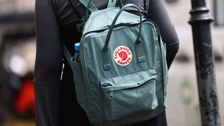 Henkilö kantaa vihreää Fjällräven Kånken -reppua, jonka sivutaskussa on sininen juomapullo.