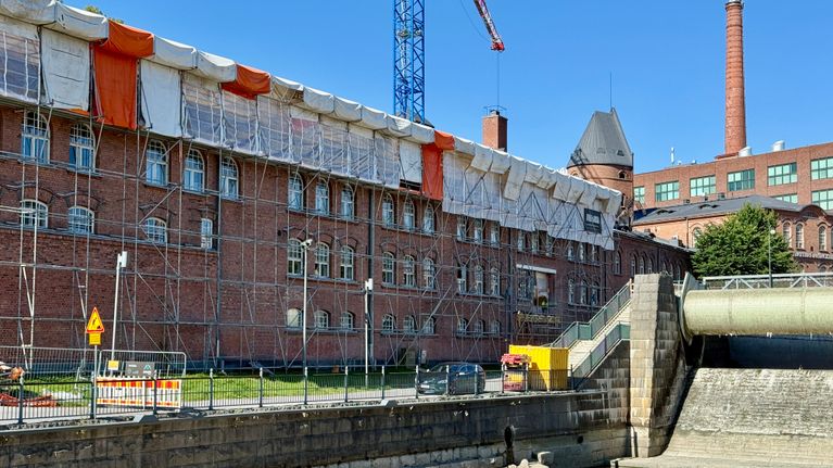 Työmaa-aluetta kuvattuna Frenckellin alueella aurinkoisena kesäpäivänä. Punatiilinen rakennus on täynnä rakennustelineitä ja taustalla kohoaa nosturi.