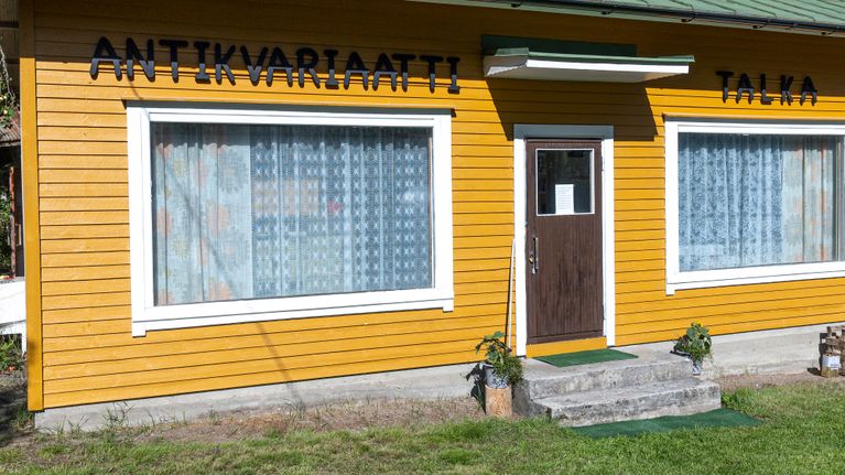 Keltainen puutalo, jonka julkisivussa on teksti "Antikvariaatti Talka". Ovi ja kaksi isoa ikkunaa etuseinällä.