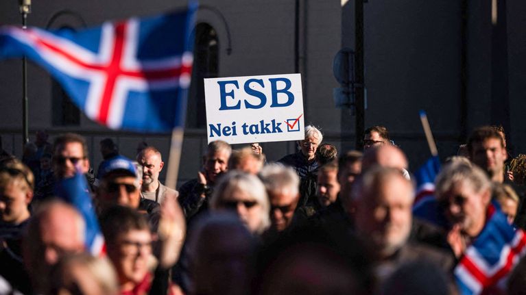 Ihmisiä kokoontuneena ulkona, Islannin lippuja ja kyltti, jossa lukee "ESB Nei takk".