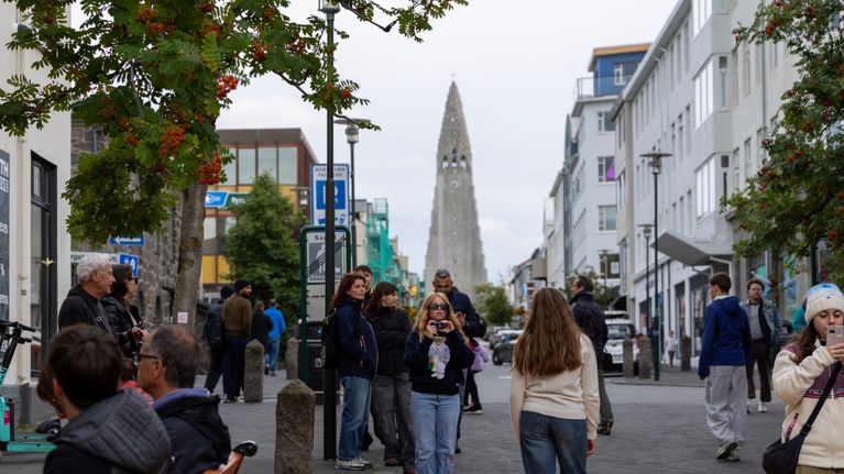 Jalankulkijoita kadulla värikkään suojatien äärellä, taustalla Hallgrímskirkja-kirkko Reykjavikissa.