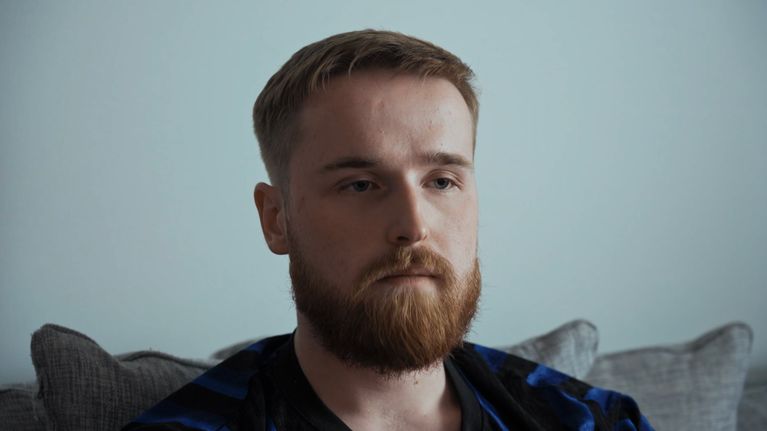 Nuori parrakas mies istuu sohvalla.