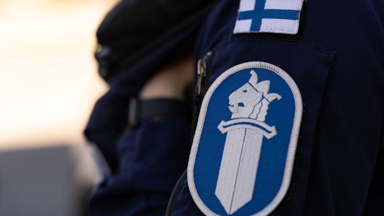 Poliisin hihamerkki, jonka yläpuolella Suomen lippu.