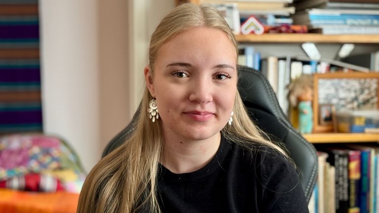 Nainen poseeraa kameralle kirjahyllyn edustalla. Ainu Feodoroff. 