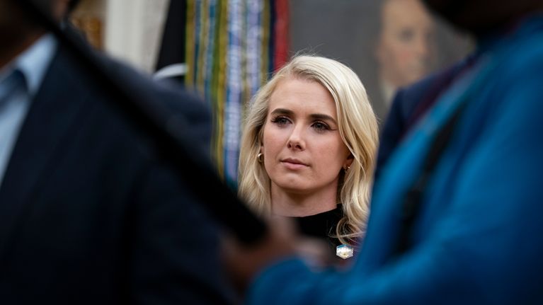 Natalie Harp, nuori vaalea nainen katsoo toisten välistä.