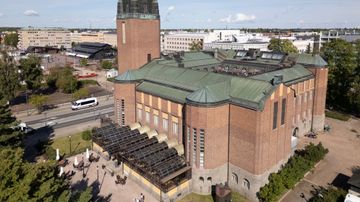 Ilmakuva ruskeatiilisestä Joensuun kaupunginteatterista, jossa torni, taustalla kaupunkia, puisto ja kauppahalli.