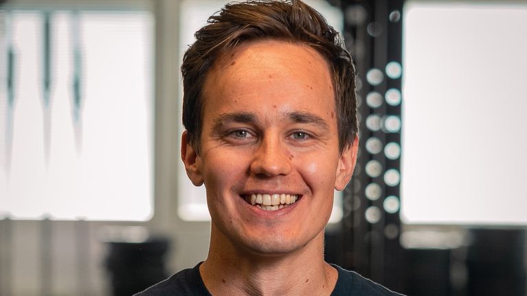 Mies katsoo suoraan kameraan ja hymyilee leveästi.