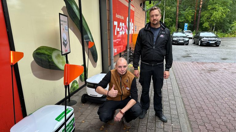 Kaksi miestä katsoo kameraan ruokarobottien keskellä.