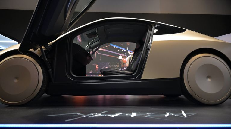 Kultainen, futuristinen auto kuvattuna sivulta. Auton ovat on avattu, ja ne nousevat edestä ylöspäin. Ohjaamossa ei istu ketään.