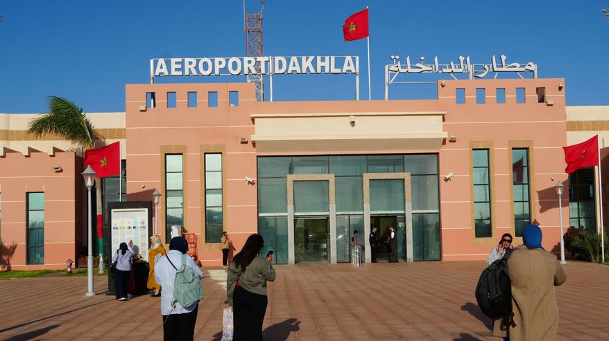 Ihmisiä seisoo Dakhlan lentokentän sisäänkäynnin edustalla, rakennuksen päädyssä teksti "Aeroport Dakhla".