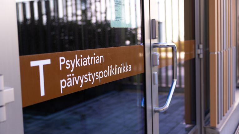 Lasioven yläreunassa on kyltti "T Psykiatrian päivystyspoliklinikka" ja ovessa kiinnitetty tiedote.