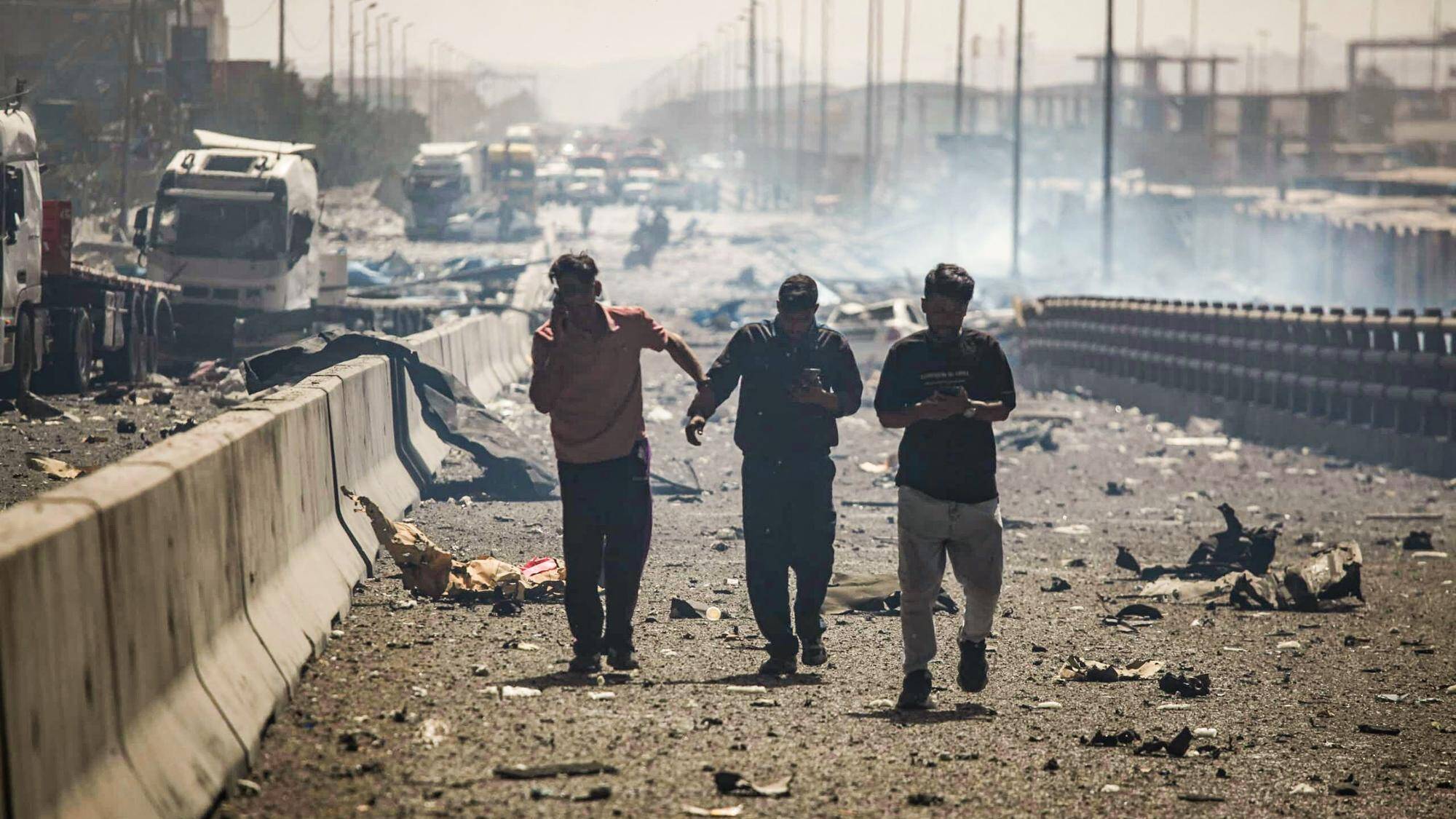 Des personnes utilisent leur téléphone alors qu'elles marchent le long d'un boulevard dévasté par une explosion au quai du port Shahid Rajaee, au sud-ouest de Bandar Abbas, le 26 avril 2025. — © MOHAMMAD RASOLE MORADI / AFP