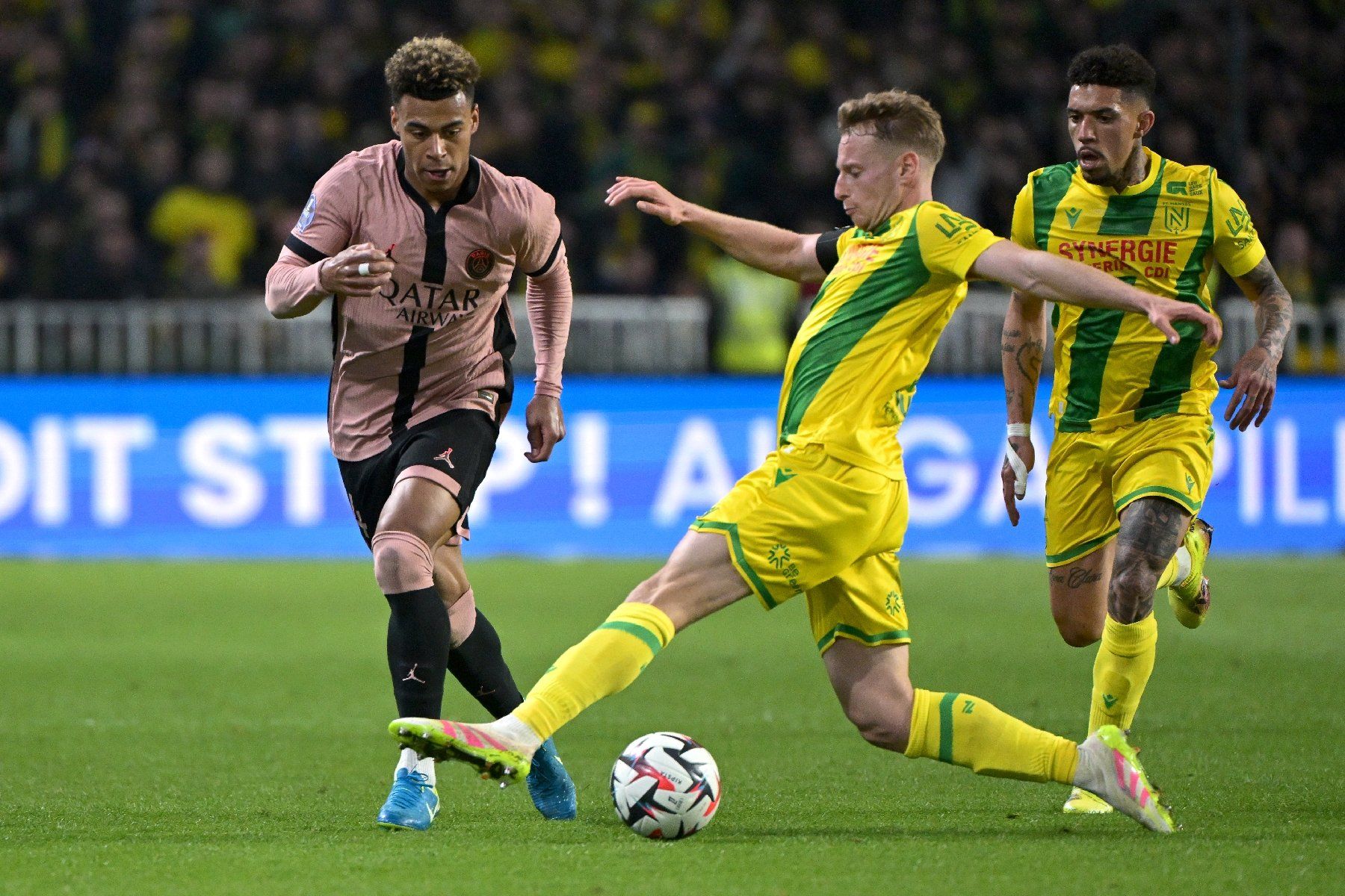 Le défenseur nantais Nicolas Cozza (C) tacle le Parisien Désiré Doué (g) lors du match nul (1-1) pour la 29e journée de Ligue 1, à Nantes le 22 avril 2025
