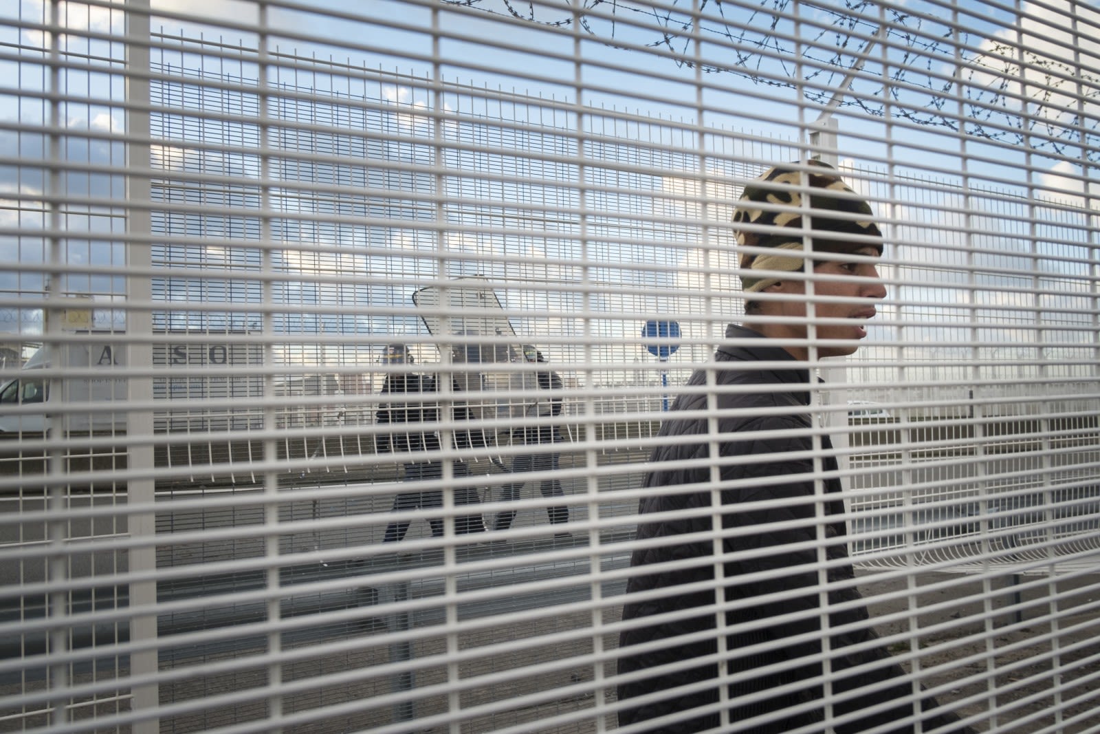 Un jeune migrant se retrouve entre les deux barrières séparant la « Jungle » de la route menant au port Ferry. Les policiers ont repoussé les migrants qui tentaient de monter dans les camions se rendant en Angleterre. Série Dougar, à Calais, entre 2015 et 2016.