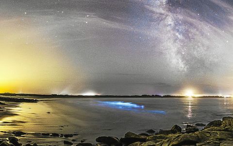 Du plancton phosphorescent (bioluminescence) dans la baie de Pors Carn, à Plomeur est visible au premier plan. Cette photo prise à partir des rochers au sud de la Pointe de la Torche, laisse apparaître la lumière orange du Guilvinec, la lumière d’une voiture au-dessus du plancton, le puissant phare d’Eckmühl et la paillote Chez Marie-Cath, juste à gauche de la lueur blanche du port de Saint-Guénolé.
